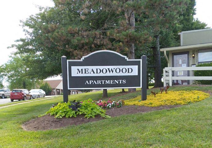 a sign for meadowood apartments in front of a yard with flowers