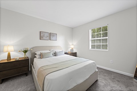 A bedroom with a large bed, two nightstands with lamps, and a window with blinds.