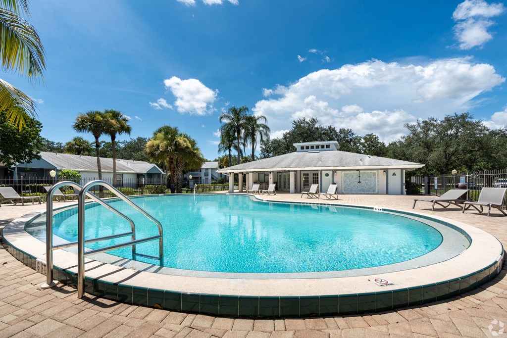 a swimming pool with chairs and a building in the background at Aqua Bay Apartments in Naples, FL 34116