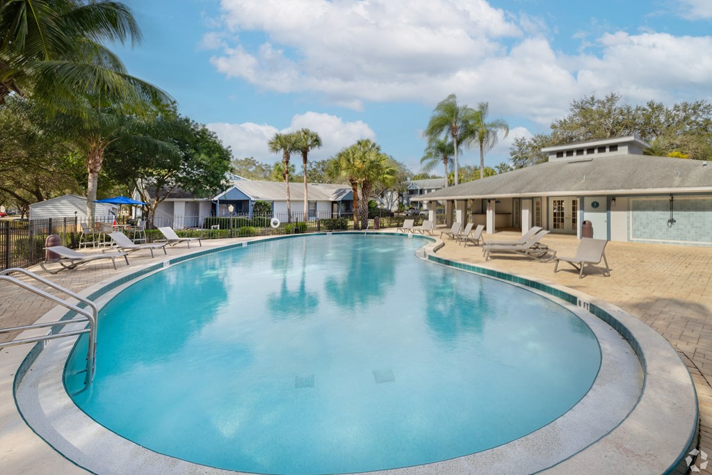 a large swimming pool with chairs and a house in the background at Aqua Bay Apartments in Naples, FL 34116