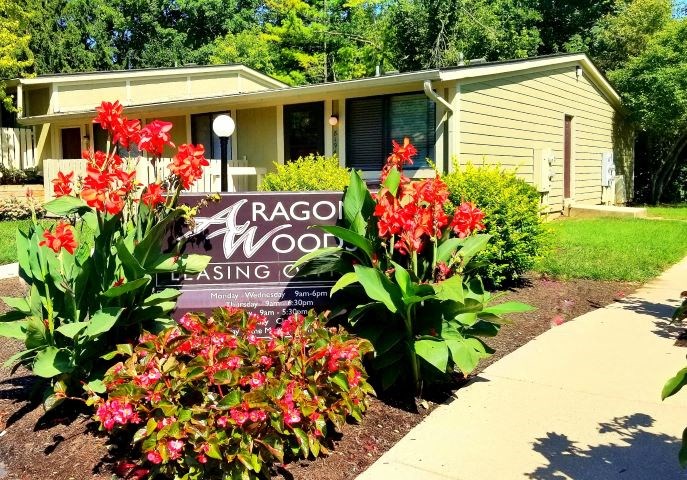 a sign in front of a house with red flowers