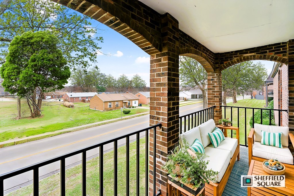 A balcony with a sofa and pillows overlooks a street.