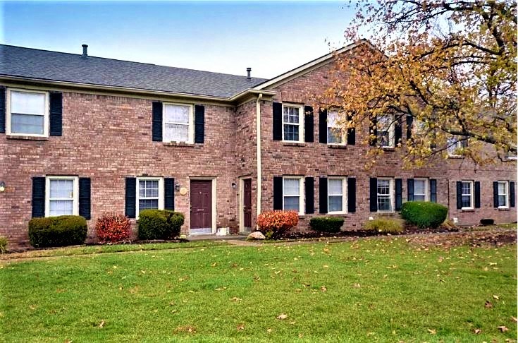 a brick house with a green lawn and a tree