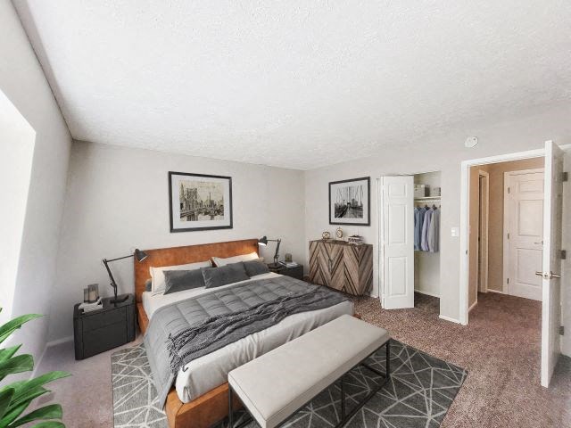 Carpeted bedroom with a closet, a bed in the middle, and a dresser. 