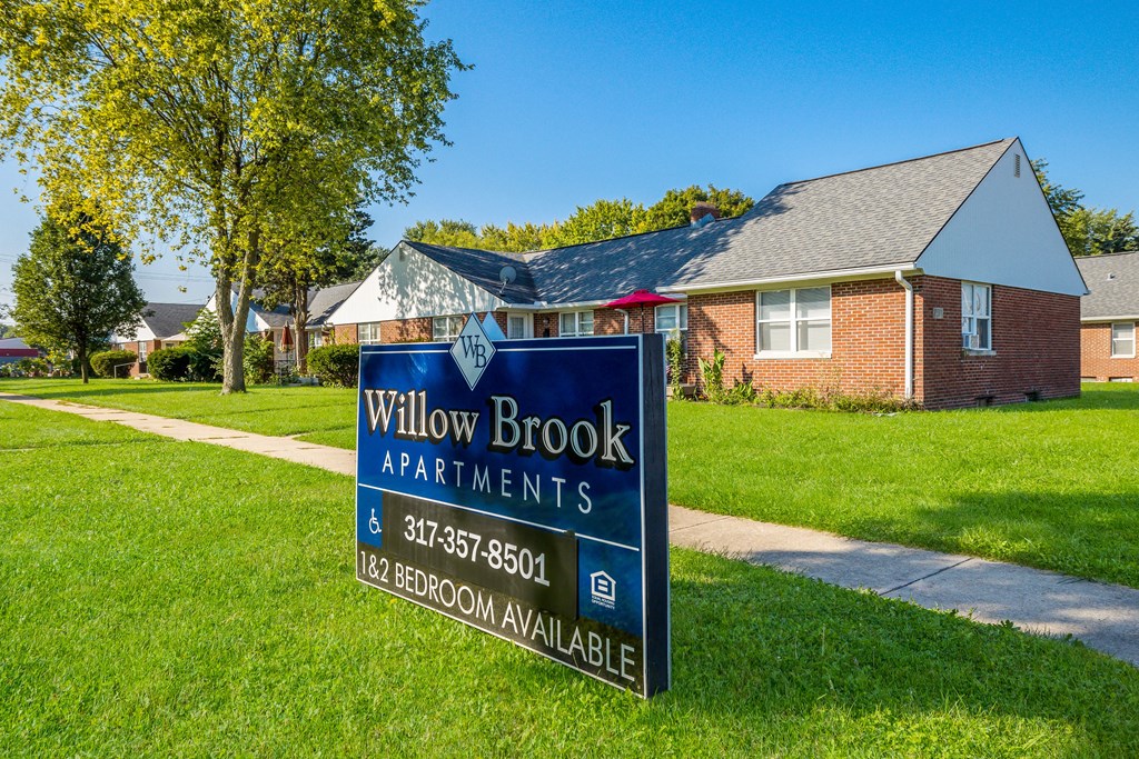 a sign for willow brook apartments in front of a house