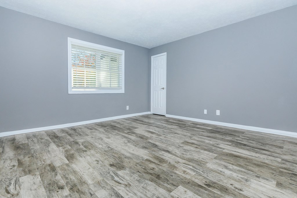 an empty room with wood floors and grey walls and a window