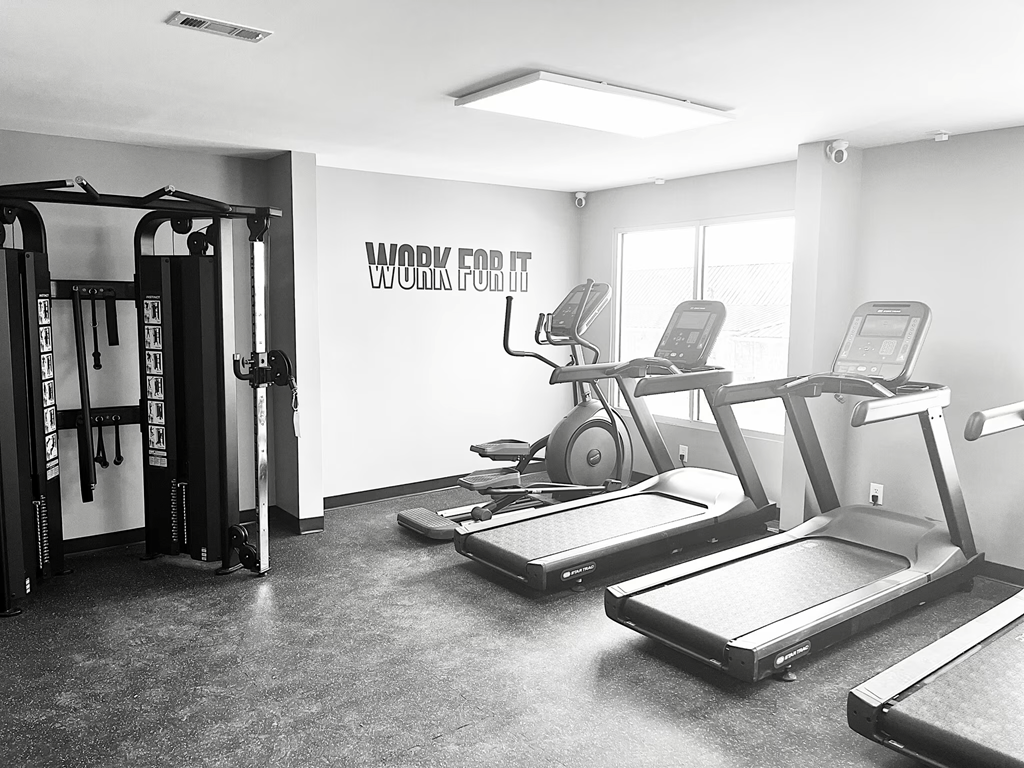 A black and white photo of a gym with treadmilers, weights, and a sign that says "Work for It".