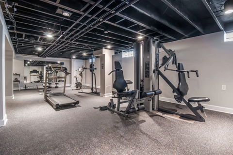 A spacious gym with a variety of equipment including a leg press machine, a chest press machine, and a bench press.