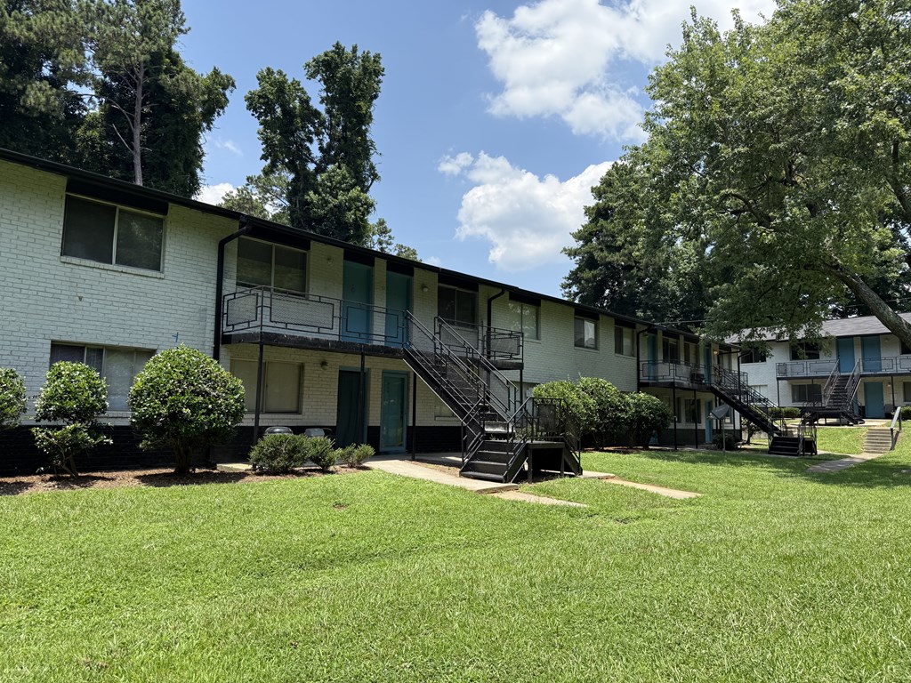 A white apartment building with green doors and black staircases.