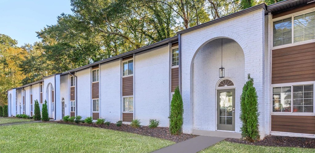 the exterior of a white brick building with a front door and a lawn