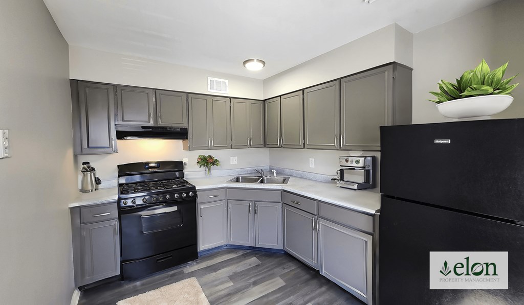 A modern kitchen with a black fridge and a plant on top.