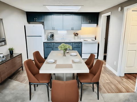 A kitchen with a table and chairs in the foreground and a refrigerator and cabinets in the background.