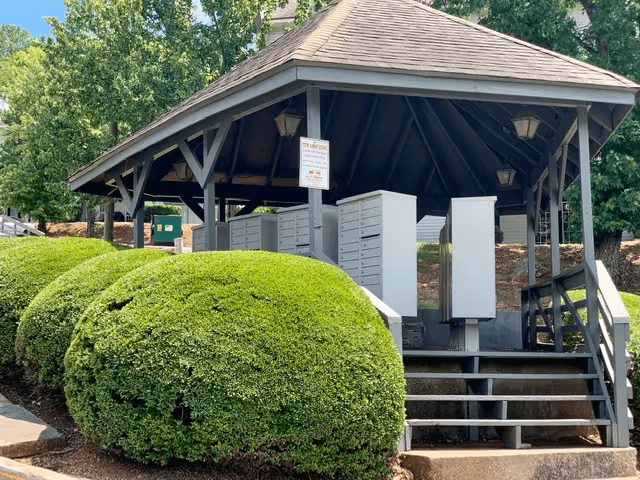 A small building with a roof and a signboard is surrounded by green bushes.