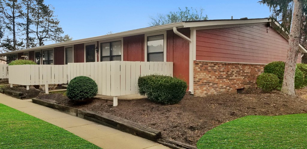 A red and white mobile home with a white fence and green bushes.