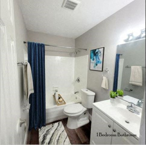 Bathroom with a bathtub, toilet, a large mirror, and sink with white cabinets. 
