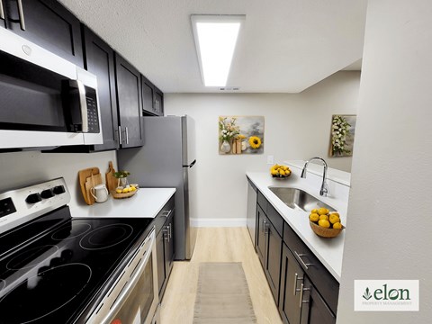 A kitchen with a stove top oven, microwave, refrigerator, and sink.