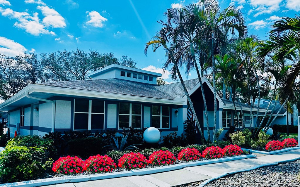 A house with palm trees and red flowers in front of it at Aqua Bay Apartments in Naples, FL 34116