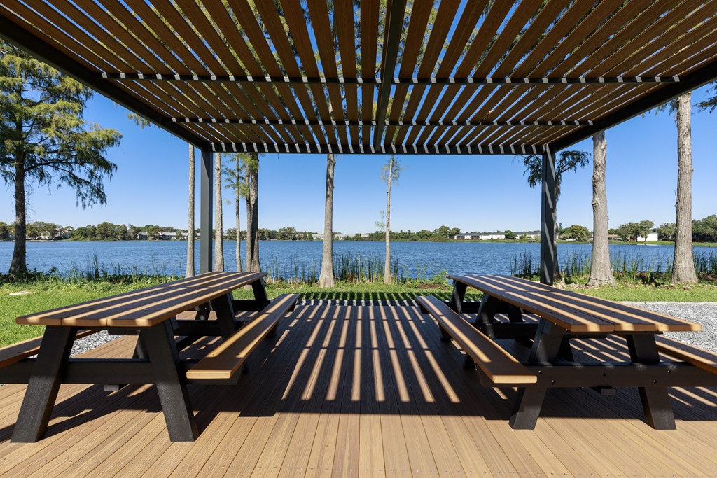 two picnic tables under a pergola overlooking a lake