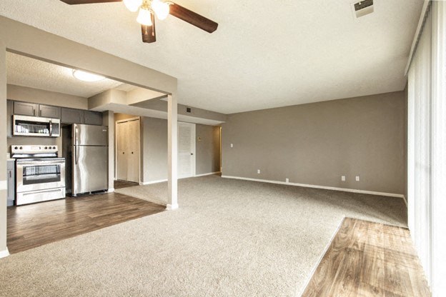 an empty living room with a kitchen and a ceiling fan