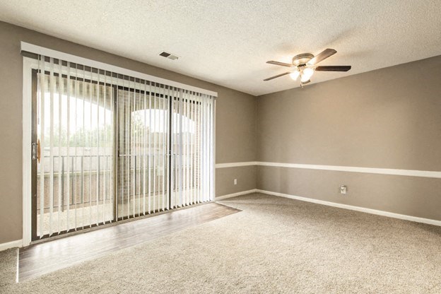 an empty living room with sliding glass doors and a ceiling fan