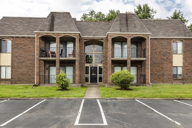 the front of a brick apartment building with a lawn and grass