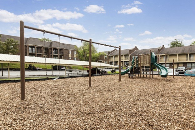 a playground with a slide and swings in front of apartments