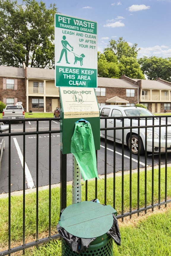 a sign on a fence with a green bag on a trash can