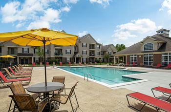 A pool area with chairs and umbrellas in front of apartment buildings.