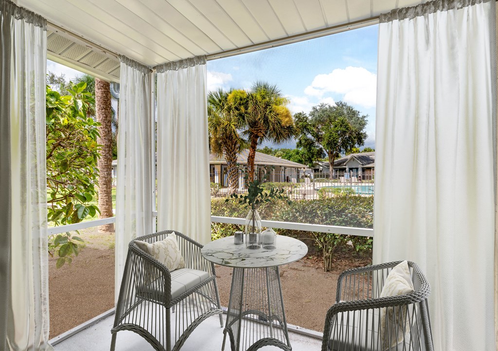 a patio with white curtains and a table and chairs at Aqua Bay Apartments in Naples, FL 34116