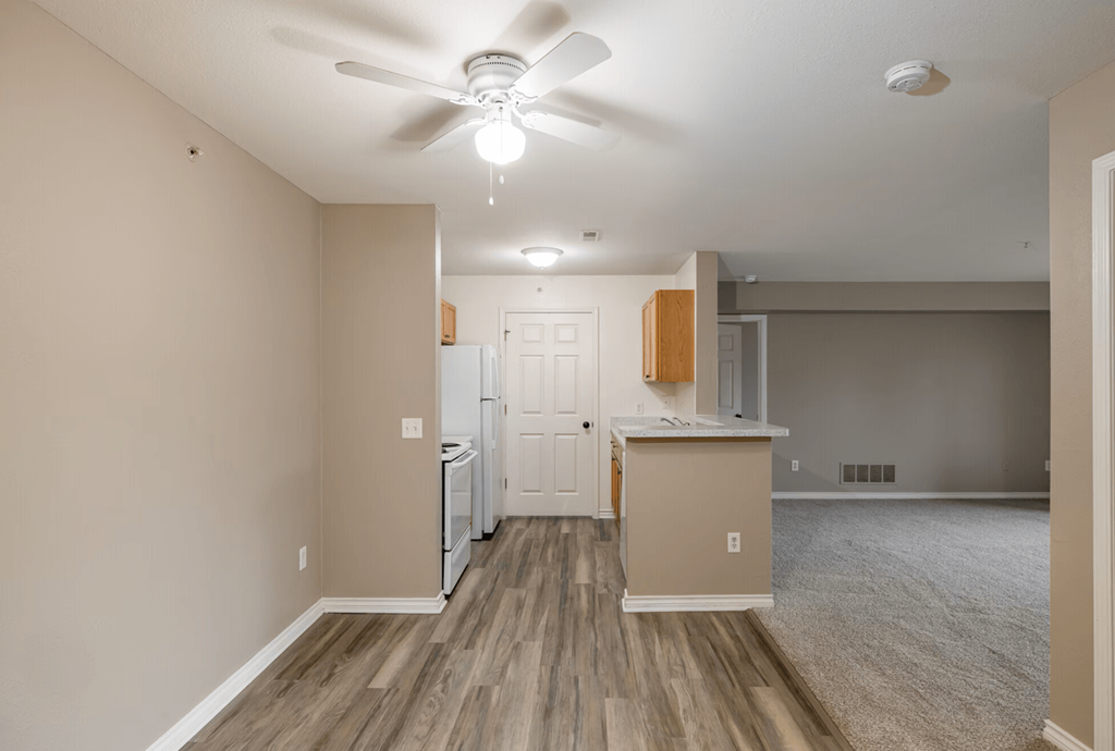 A room with a ceiling fan and a kitchenette.