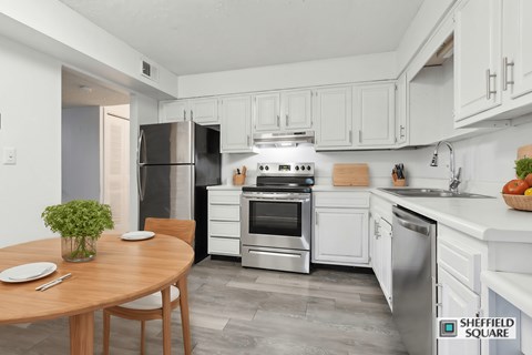 A kitchen with a table and chairs in the foreground and a refrigerator, oven, and sink in the background.