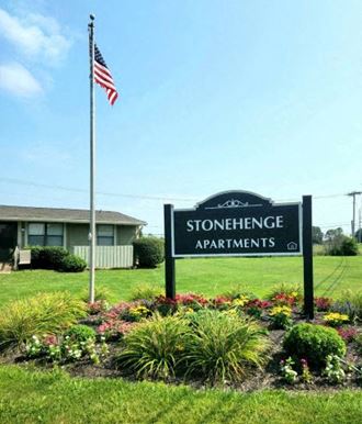 a sign for stonehenge apartments in front of a flag