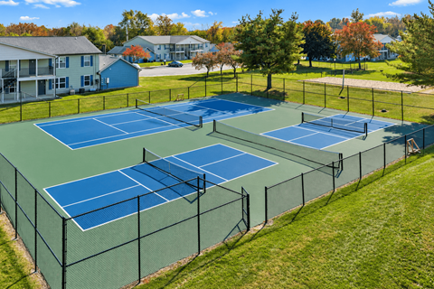 A tennis court surrounded by a fence with trees and houses in the background.