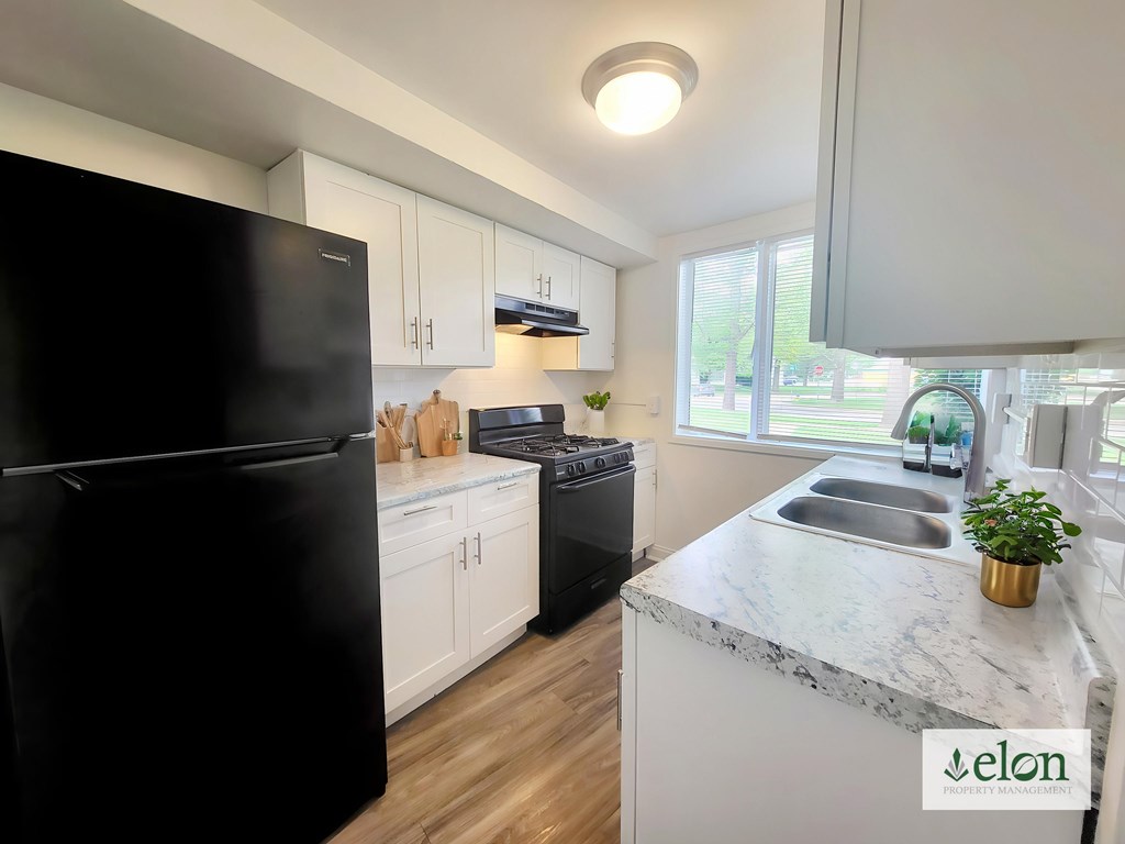 A kitchen with a black fridge, white cabinets, and a marble countertop at Townhomes at 28th, Columbus, Indiana