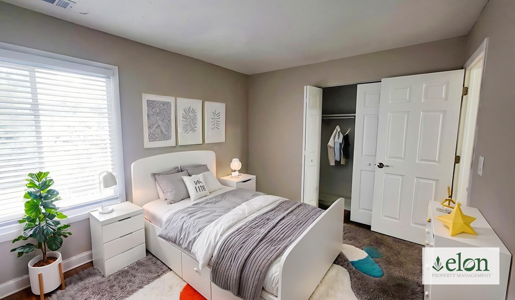 A bedroom with a bed, nightstand, and a plant.