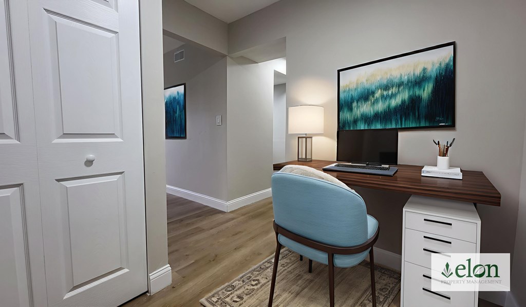 A room with a desk, chair, and a painting on the wall.