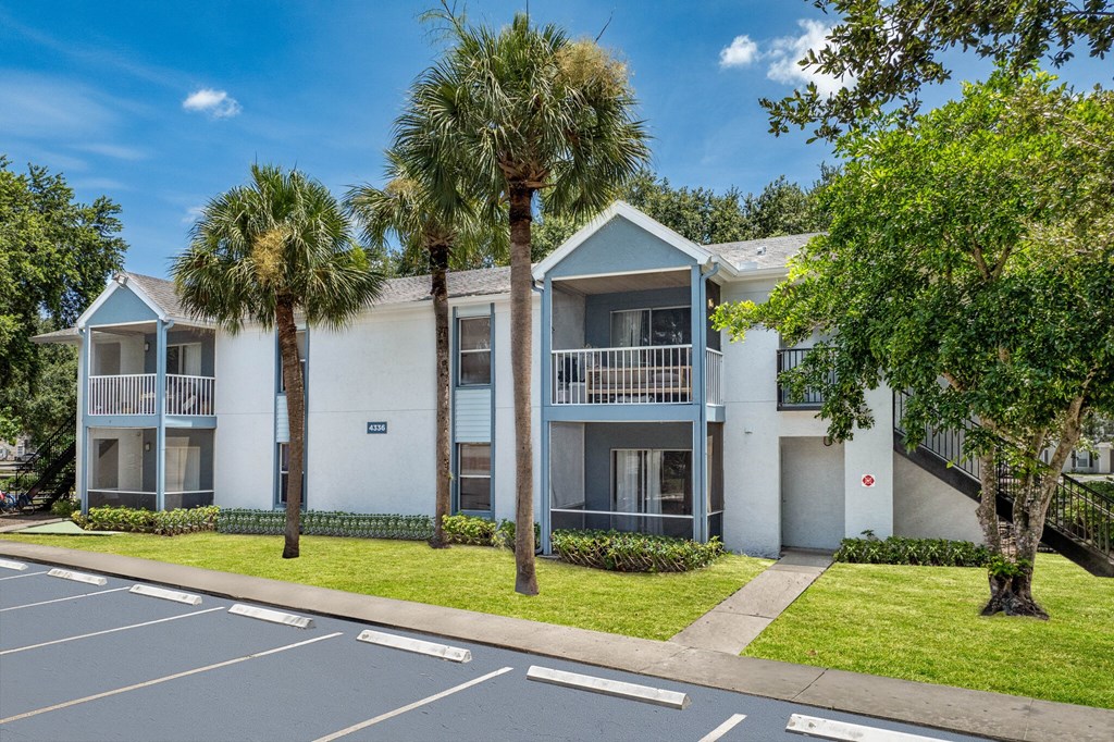 a white apartment building with palm trees in front of it at Aqua Bay Apartments in Naples, FL 34116