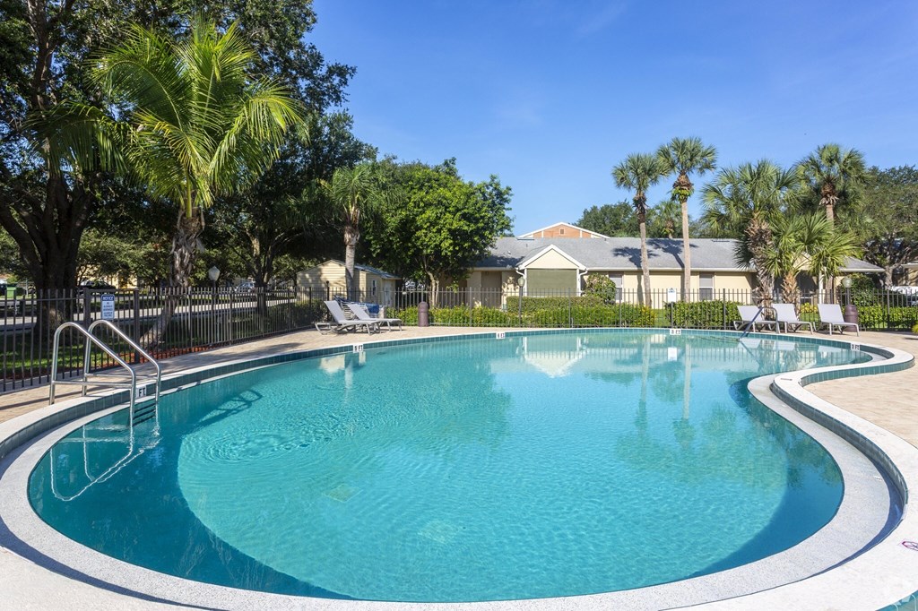 a swimming pool with palm trees and a house in the background at Aqua Bay Apartments in Naples, FL 34116