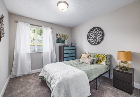 A bedroom with a bed, nightstand, and window with white curtains.