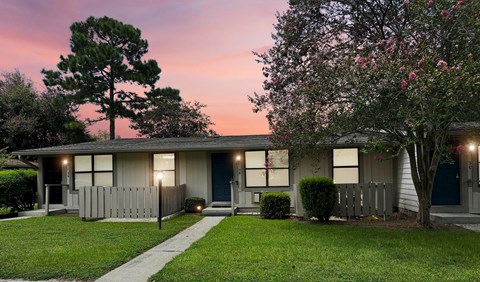 A house with a blue door and a tree with pink flowers in front.