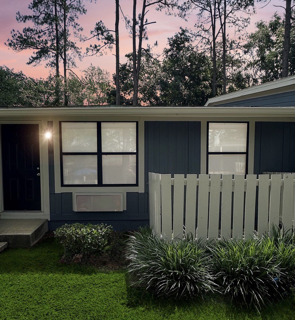 A house with a white picket fence and green plants in front.