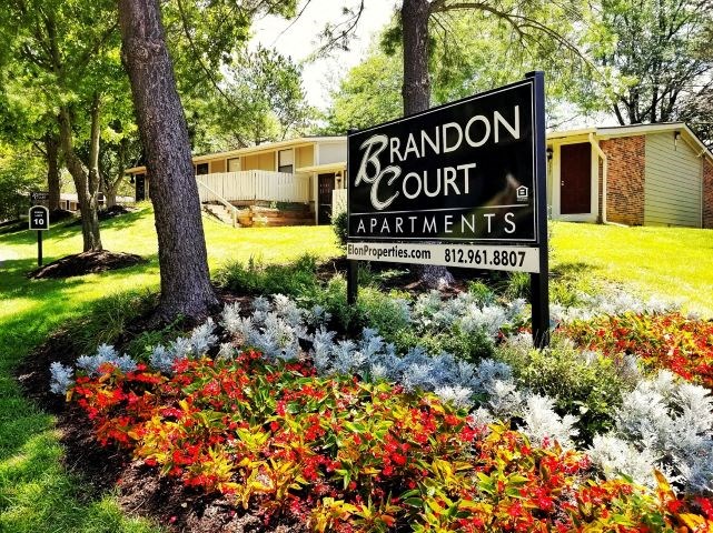 a sign for grand court apartments in front of a yard with flowers
