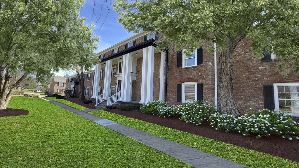 A building with a brick facade and a white trim is surrounded by a well-manicured lawn and trees.
