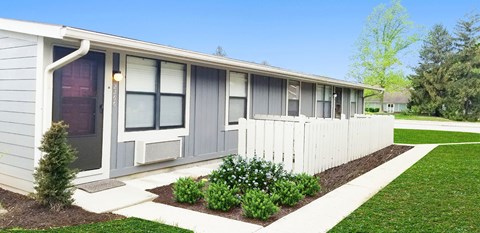 A small building with a grey siding and a white picket fence.