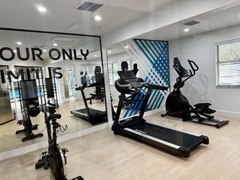 a gym with cardio equipment and a large window with your only limits signage on it