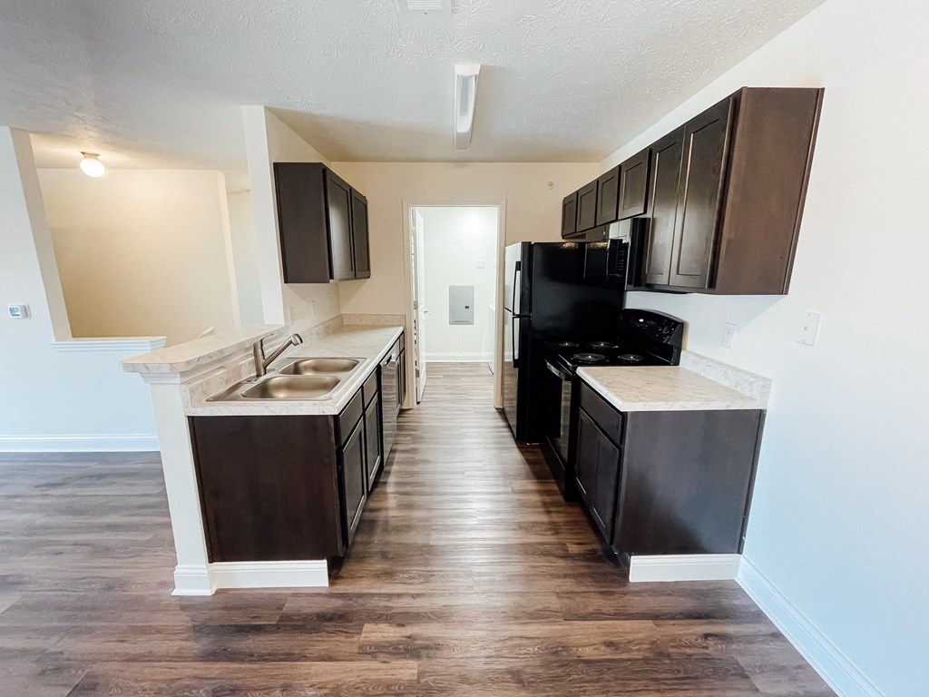 an empty kitchen with black appliances and wooden floors