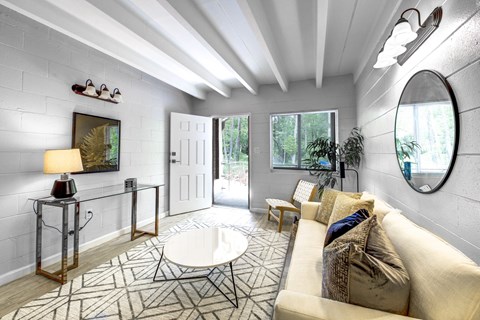 A well-lit living room with a white couch and a round mirror on the wall.