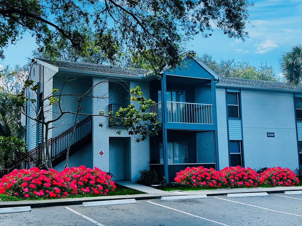 A blue apartment building with a parking lot and flowers at Aqua Bay Apartments in Naples, FL 34116