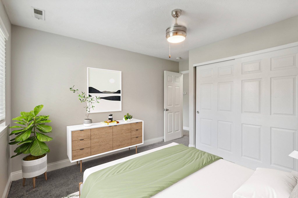 A bedroom with a bed, dresser, and a potted plant.