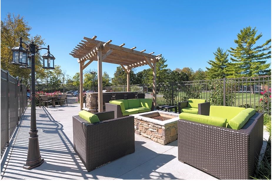 A sunny day at the park with a wooden pergola and green cushioned seating.